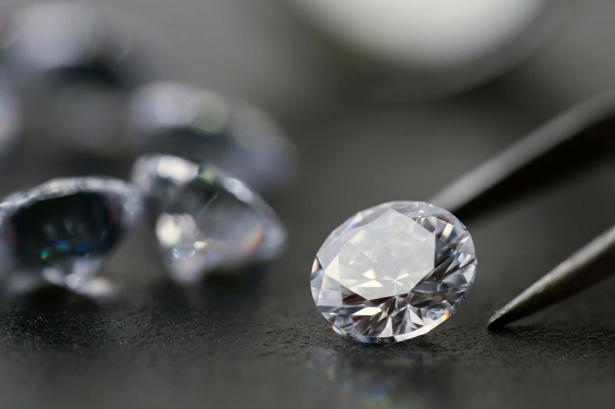 Diamante y pinzas de joyero, diamantes de fondo borrosos, fondo gris, alta calidad, joyería.